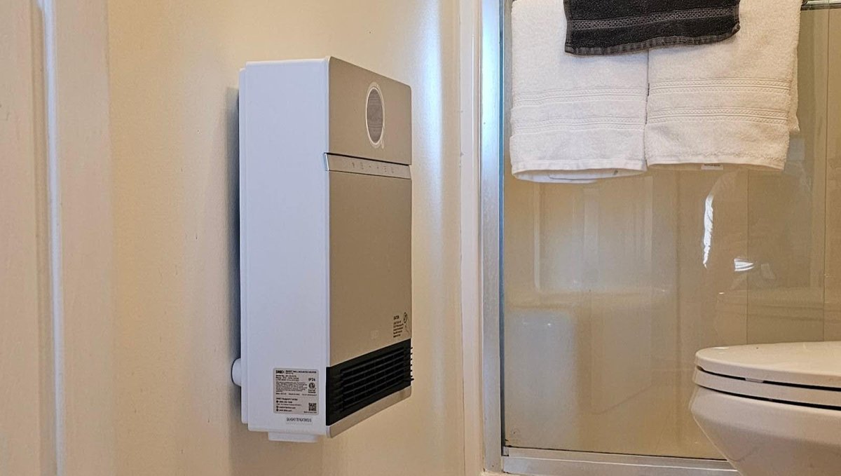 A modern electric bathroom heater installed on a tiled wall in a bright bathroom.